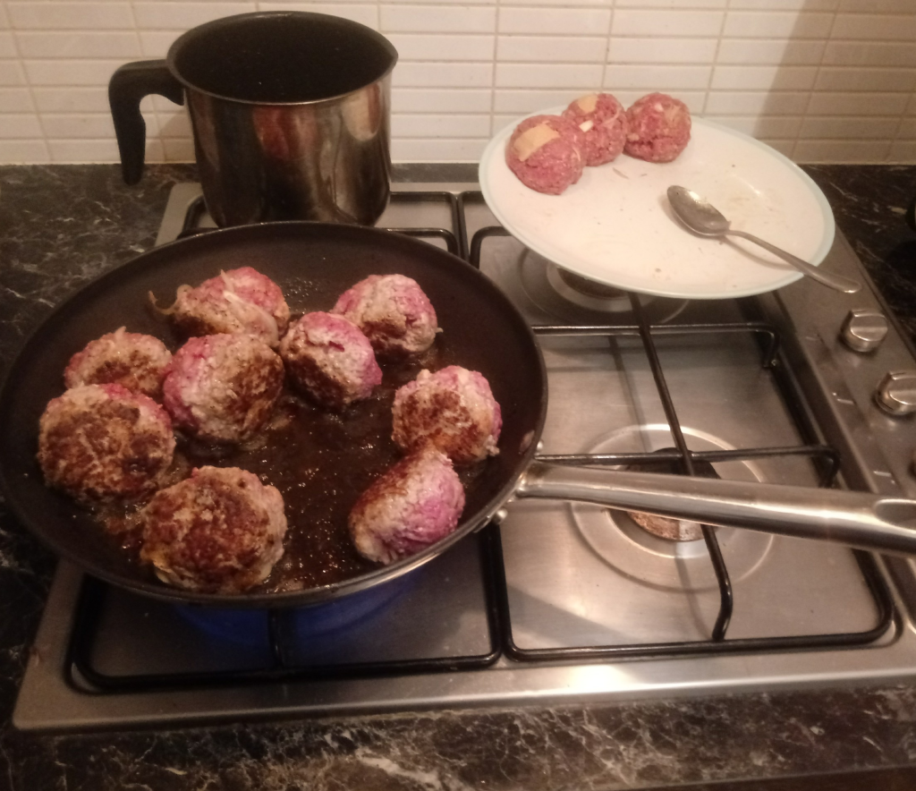 A large frying pan of part-cooked Swedish meatballs and a plate of raw meatballs